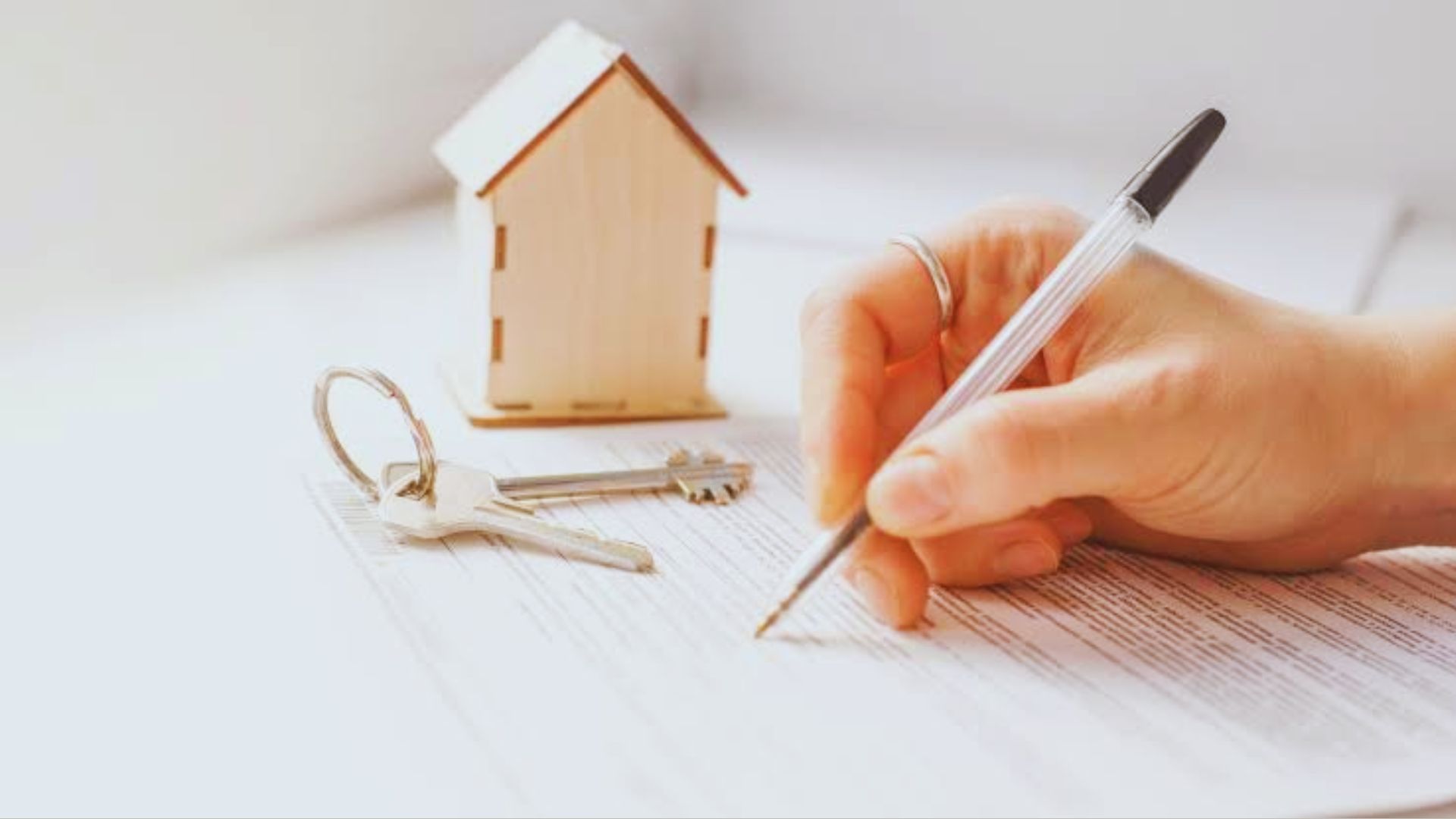 A person signing a contract with a house model nearby illustrating state deed requirement differences.