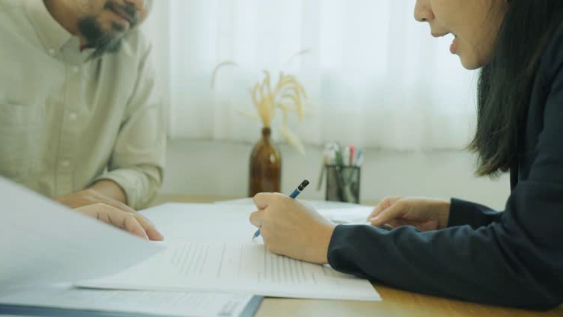 Woman signing legal contract while man explains documents at desk, business agreement consultation