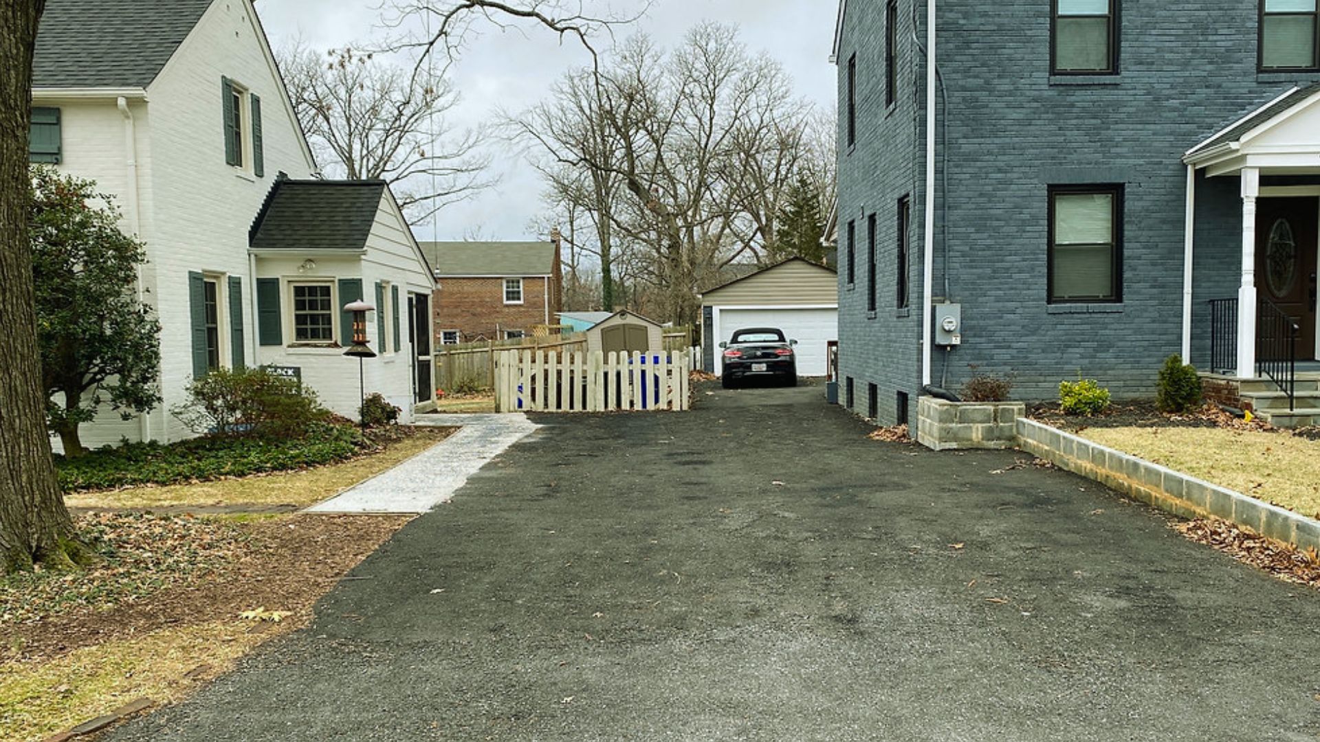 Shared asphalt driveway easement between neighboring houses with white picket fence, garages, and parked car showing property access