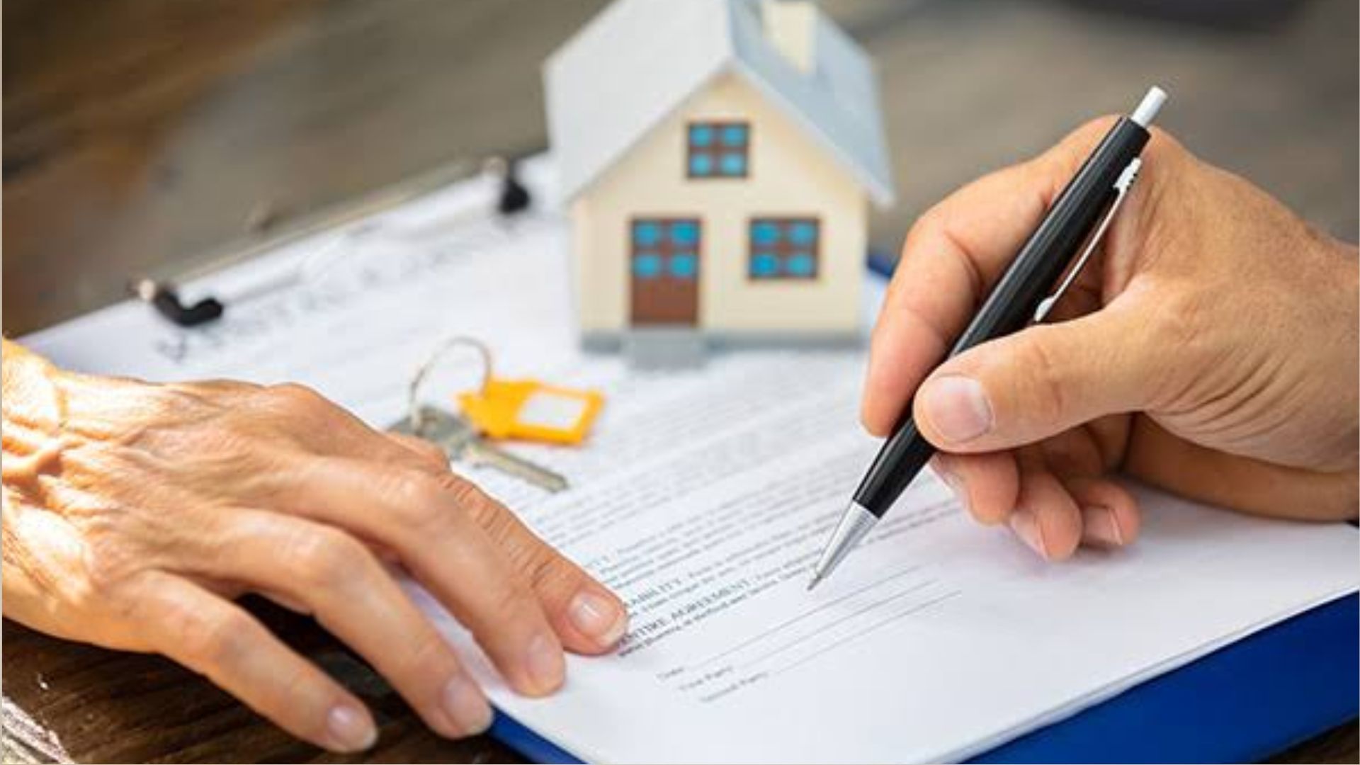 Close-up of hands signing property agreement on clipboard, with small model house and house keys with yellow tag.
