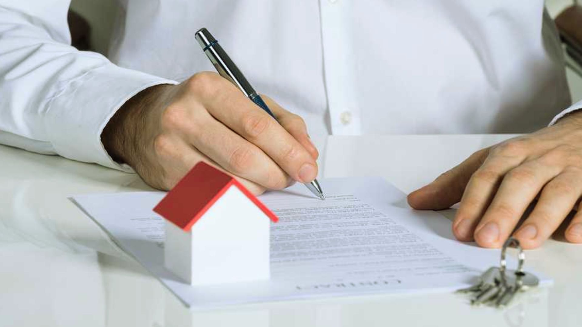 Person signing quitclaim deed property contract with red roof model house and keys on desk