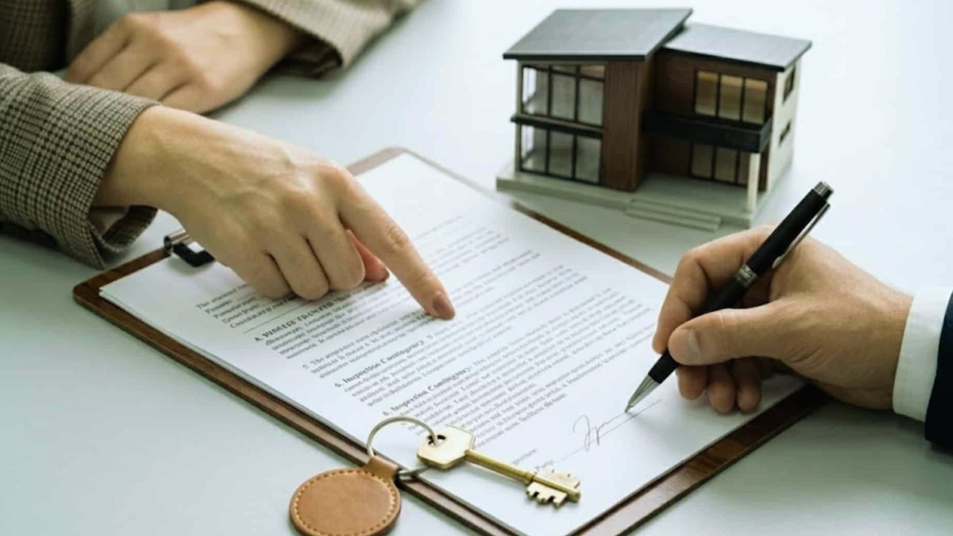 Buyer signing quitclaim deed property transfer contract with house model and keys on desk