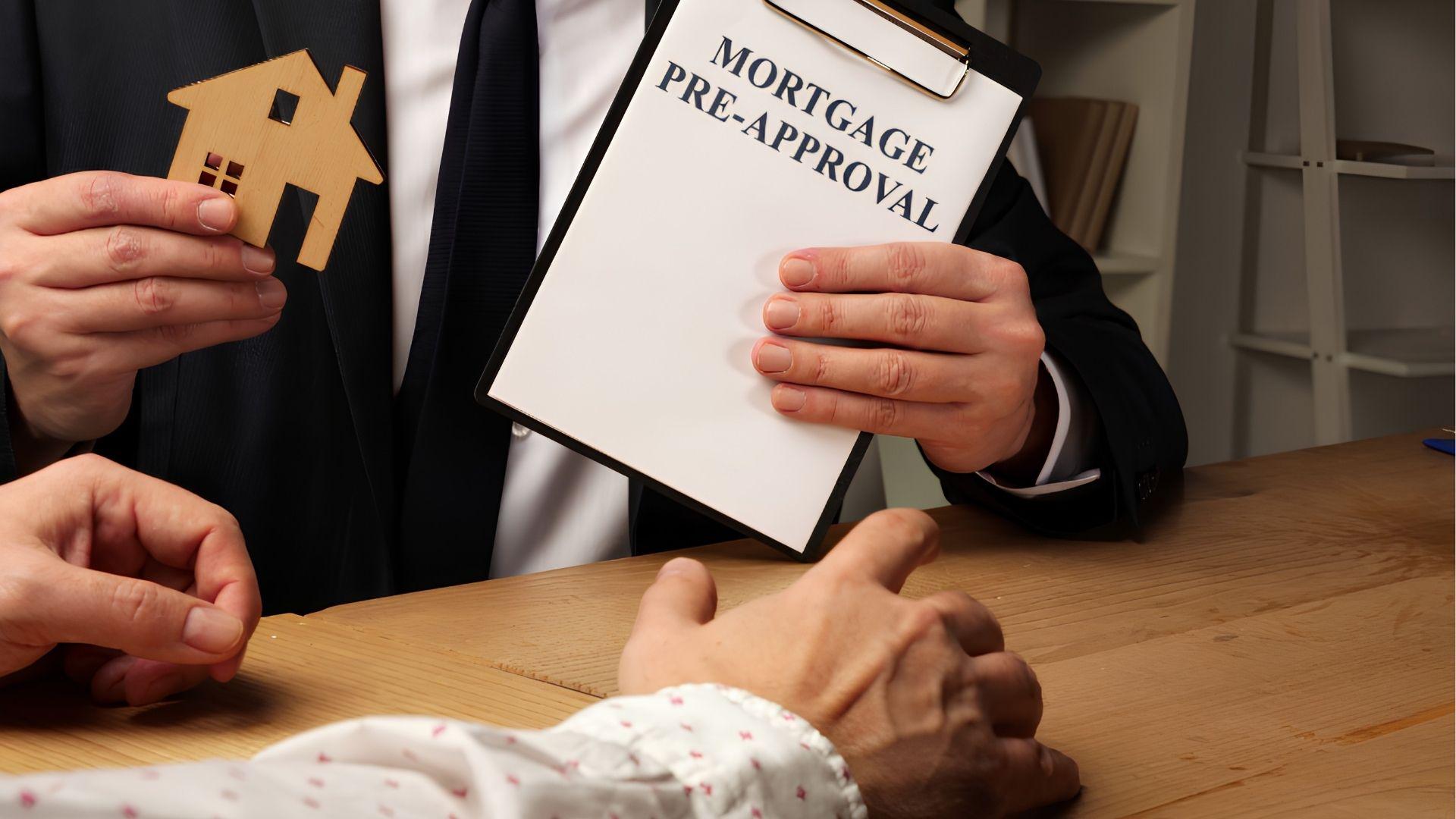 Agent holding a Mortgage Pre-Approval clipboard and wooden house across a desk