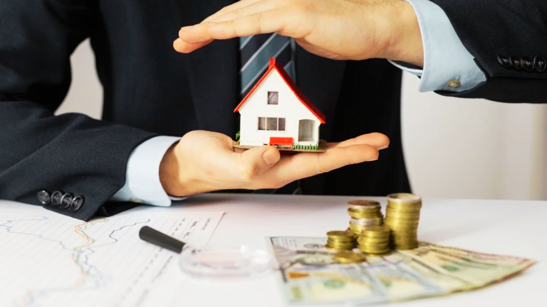 A suited man displays a house model and coins, representing the concept of community property trusts and their advantages.