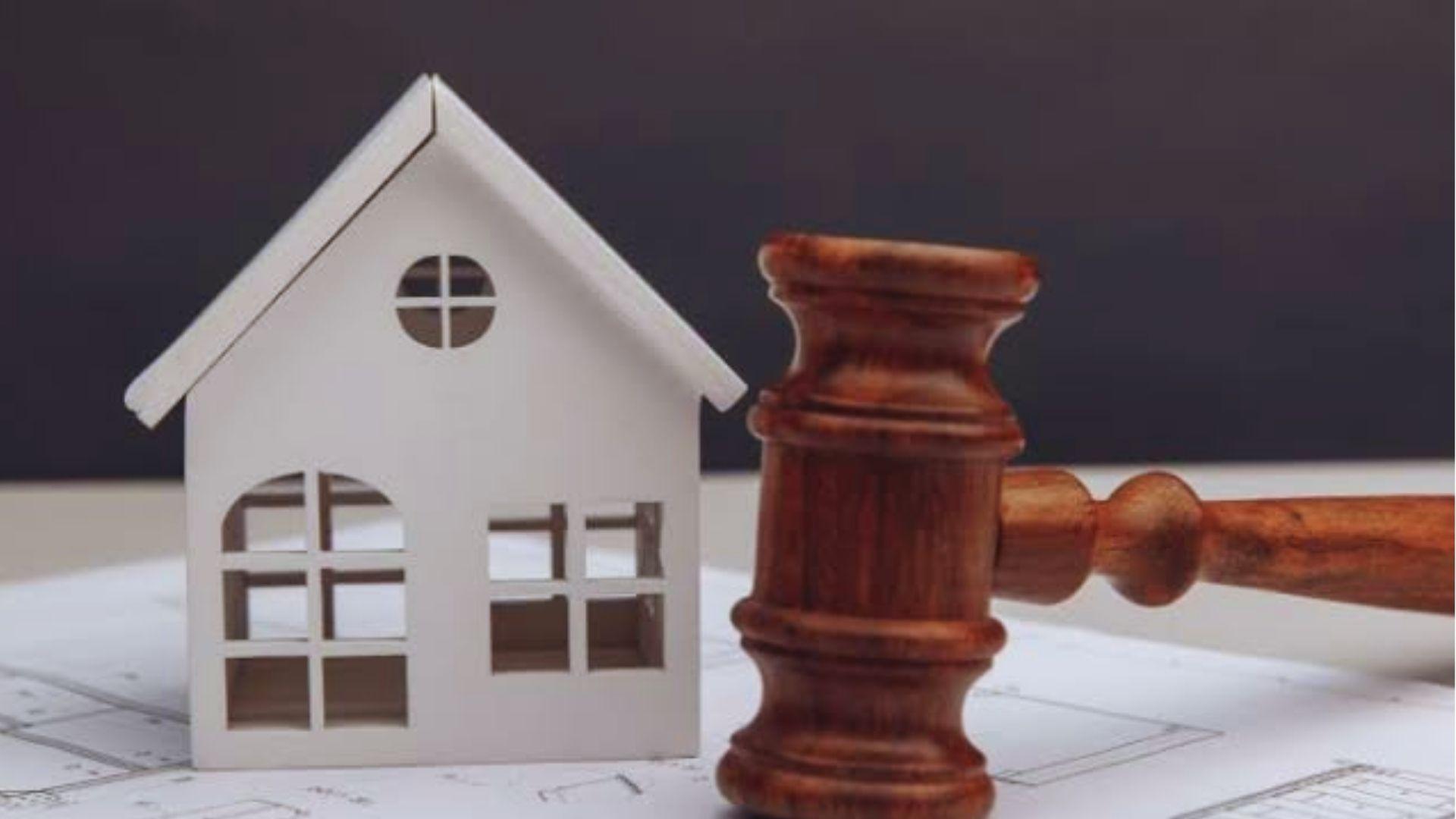 White wooden model house next to a brown wooden gavel resting on architectural blueprints.