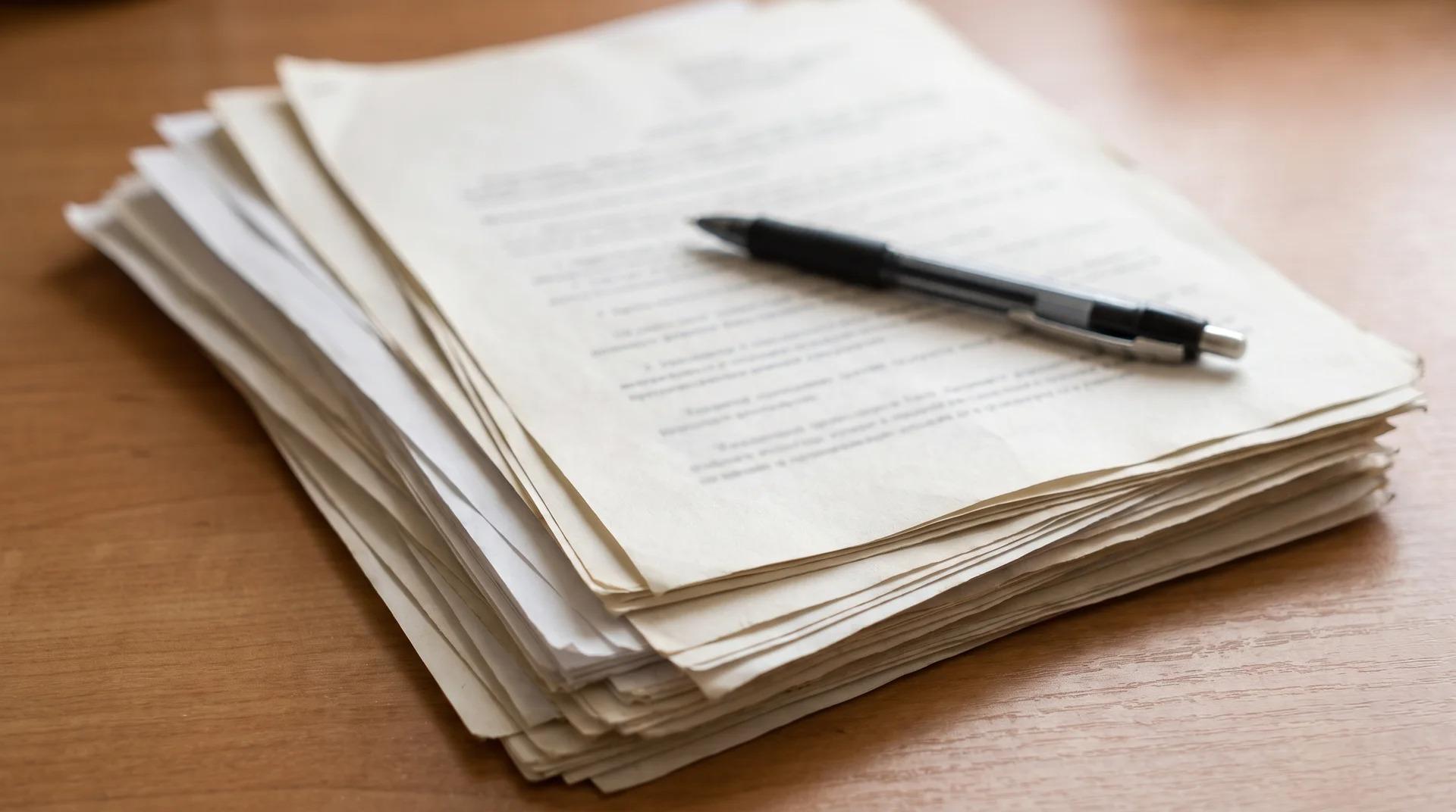 A stack of papers with a pen resting on top, arranged on a desk