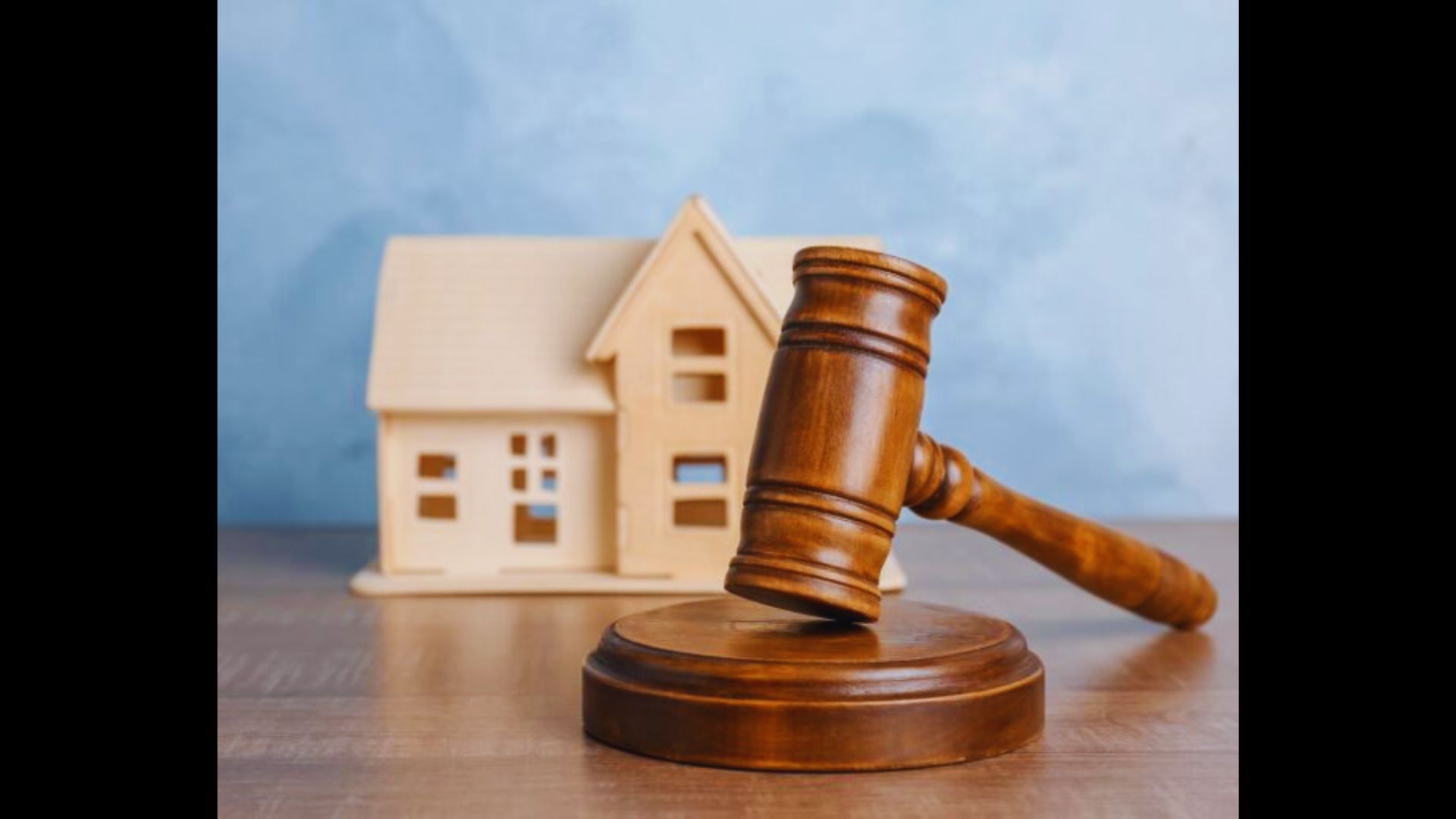 A wooden judge's gavel resting next to a miniature model house on a wooden surface.
