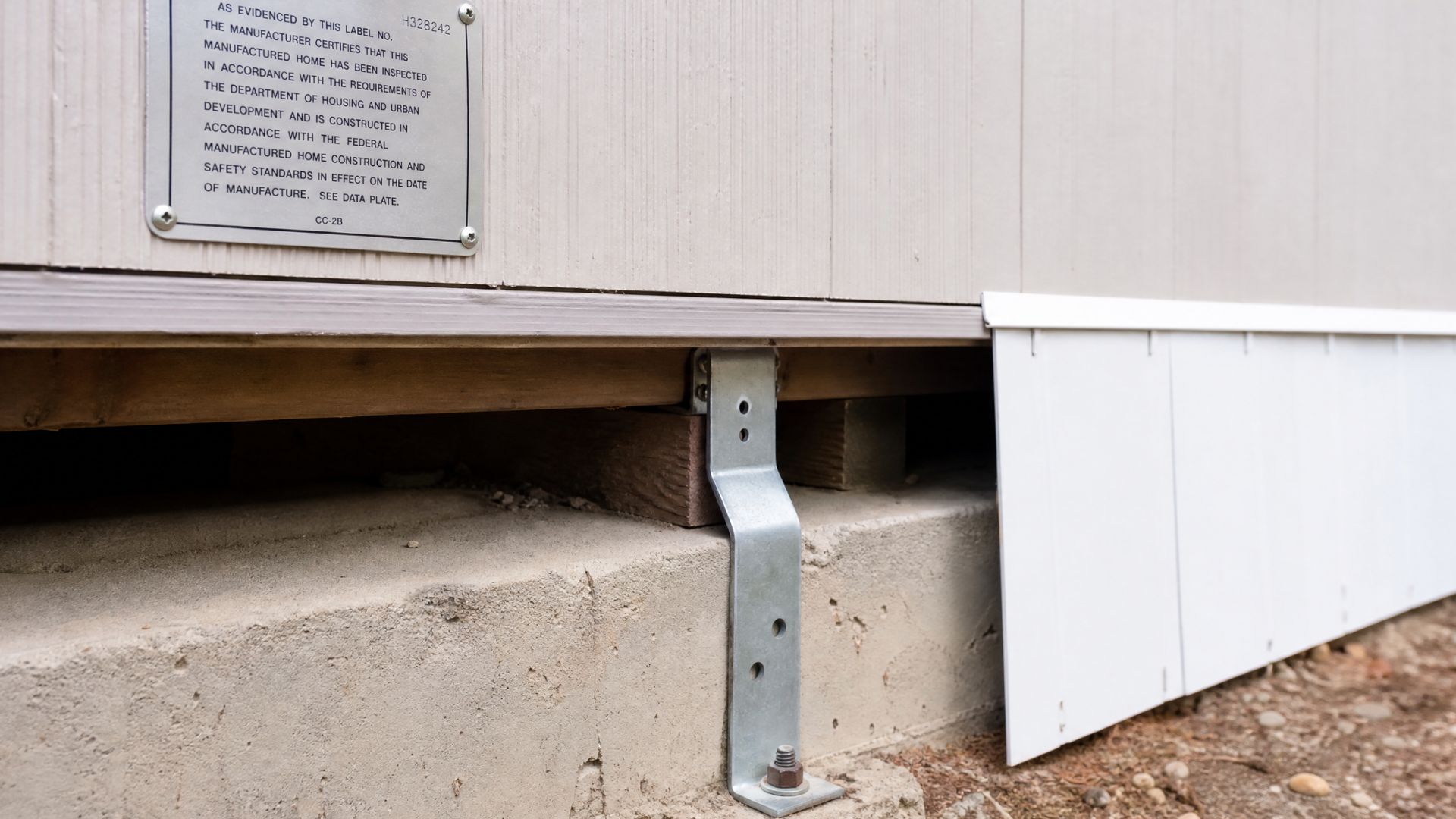 Manufactured home foundation with metal tie-down strap and certification label near the baseFile name-manufactured-home-foundation-requirements