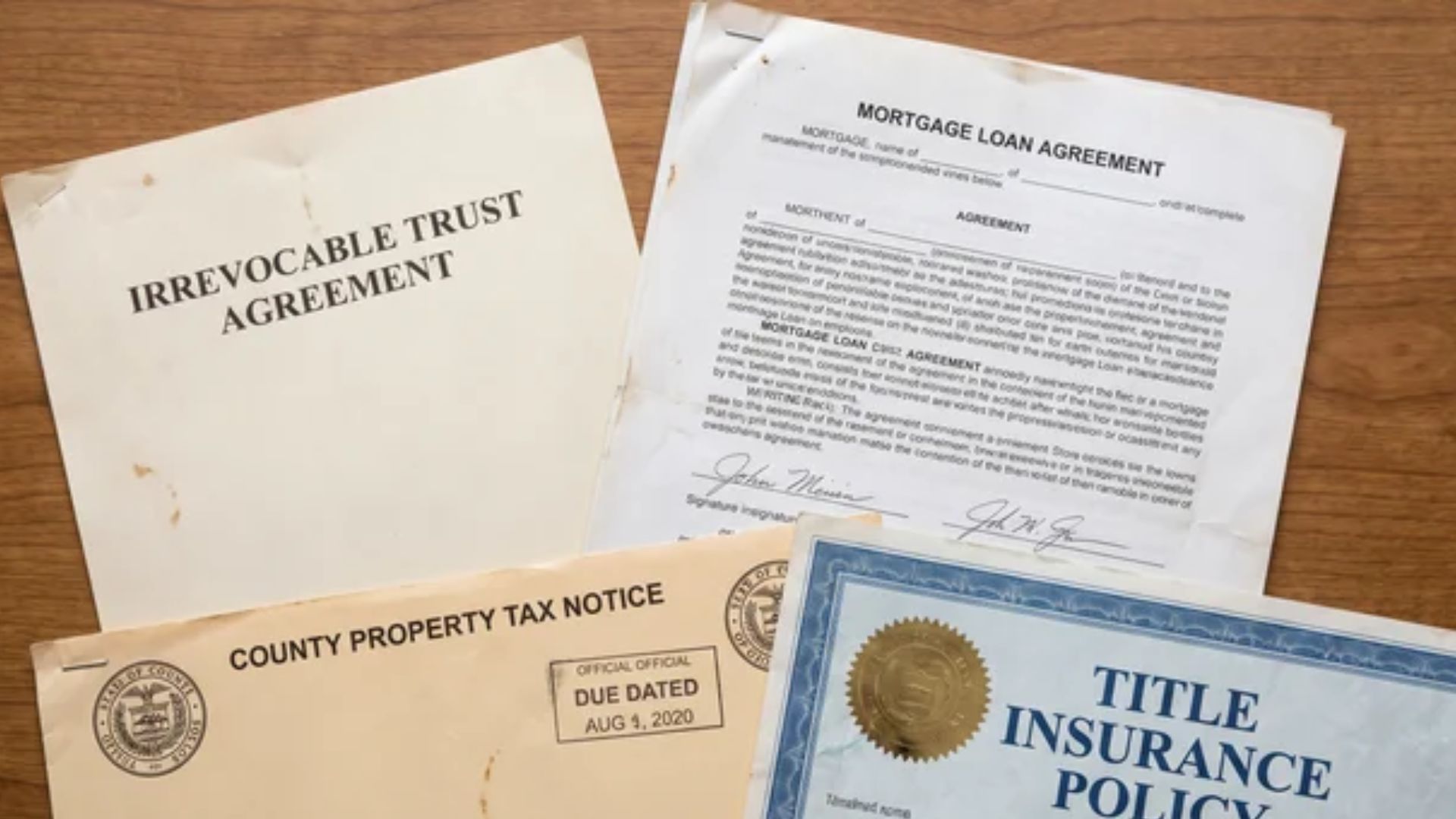 Trust document, mortgage agreement, property tax notice, and title insurance policy arranged on a flat surfaceFile Name: mortgaged-house-trust-downside-documents