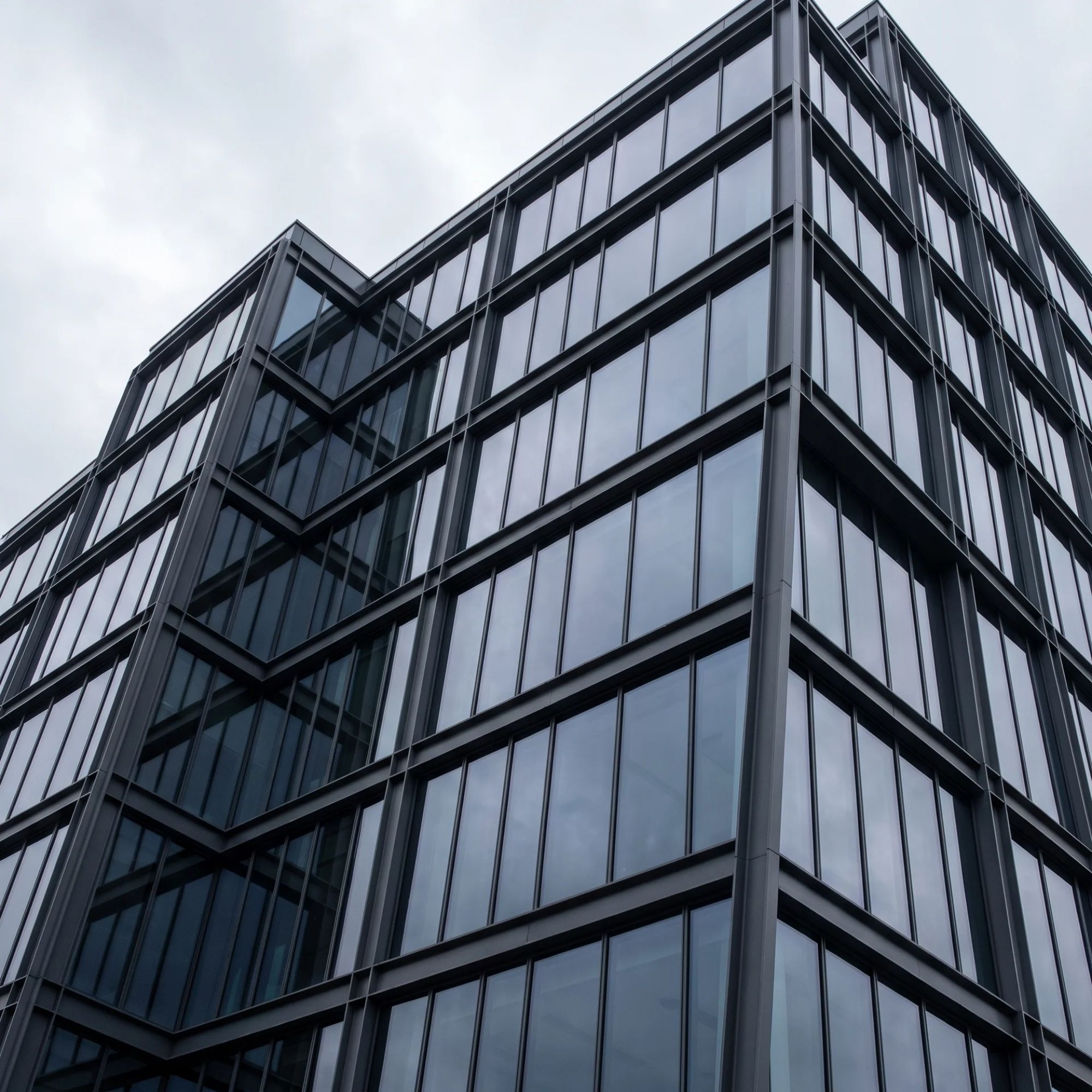 Dark glass and steel commercial building facade with geometric grid panelling viewed from below